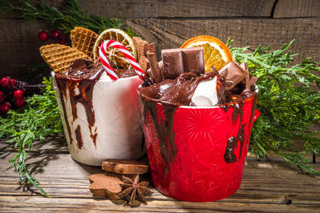 Christmas styled overloaded hot chocolate mugs with various toppings - chocolate slices, spices, sweets, cookies, candy and gingerbreads, wooden cozy winter background copy spaceの写真素材