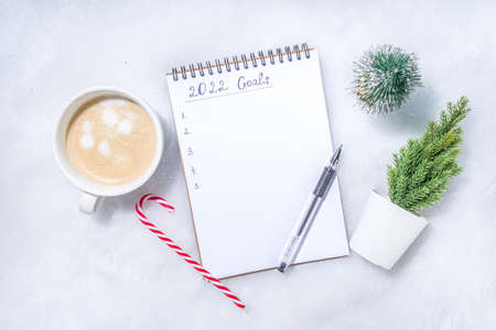 2022 new year goals concept. Year plan and action list on notepad with holiday decoration, latte coffee cup on white fluffy background flatlay top view copy spaceの写真素材