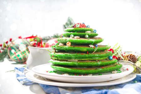 Stack of green colored breakfast pancakes, like Christmas tree with sugar sprinkles. Festive Christmas breakfast on Xmas and New Year decorated tableの写真素材