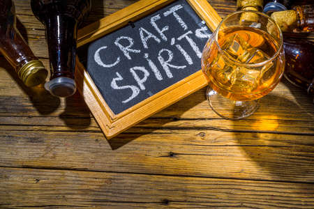 Craft spirit alcohol. Various bottles and glass with hand crafted hard strong alcohol drinks. Old wooden rustic background copy spaceの写真素材