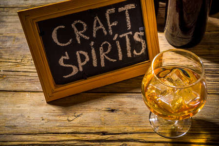 Craft spirit alcohol. Various bottles and glass with hand crafted hard strong alcohol drinks. Old wooden rustic background copy spaceの写真素材