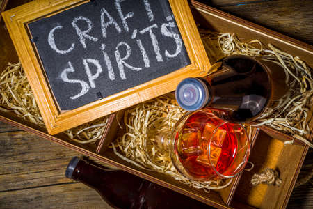 Craft spirit alcohol. Various bottles and glass with hand crafted hard strong alcohol drinks. Old wooden rustic background copy spaceの写真素材