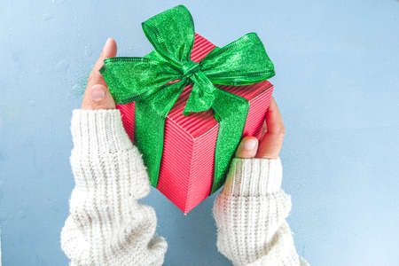 Female hands hold big red gift box glittering green tied ribbon bow on light blue background, copy space. Girl hands with present box. Christmas, New Year winter holidays Birthday presentの写真素材