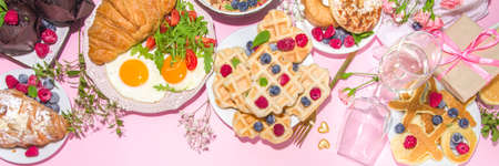 Valentine day brunch menu background with various breakfast and lunch dishes, waffle, growing, muffins, donuts, berries, fries scrambled eggs, pancakes, pink background copy spaceの写真素材