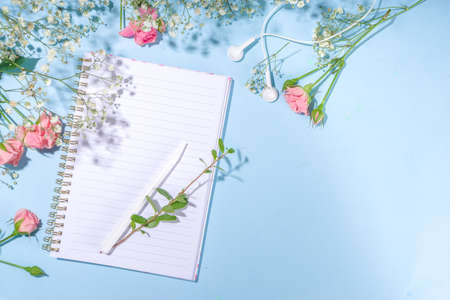 Cute spring flatlay with flowers and green spring leaves, high-colored bright sunny blue background with clean notepad pages for your text, top view frameの写真素材