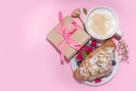 Croissant with coffee and Valentines gift and coffee latte mug on pink background copy space. Valentine day, Mother day sweet tasty breakfast idea. Good morning and nice spring, summer day conceptの写真素材