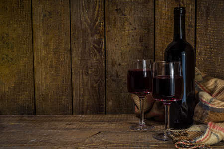 Winter wine tasting degustation background. Craft wine bottle with two glasses over wooden background with cozy plaid and winter decoration copy spaceの写真素材