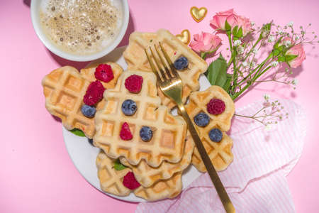 Heart shaped Valentines waffles, with berry and coffee latte mug on pink background copy space. Valentine day, Mother day sweet tasty breakfast ideaの写真素材