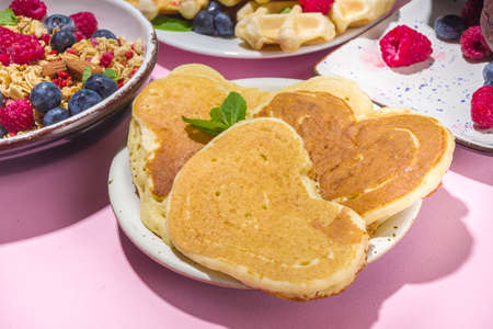 Valentine day brunch menu background with various breakfast and lunch dishes, waffle, growing, muffins, donuts, berries, fries scrambled eggs, pancakes, pink background copy spaceの写真素材
