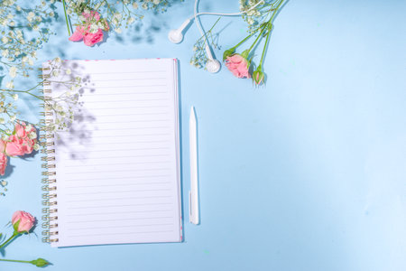Cute spring flatlay with flowers and green spring leaves, high-colored bright sunny blue background with clean notepad pages for your text, top view frameの写真素材