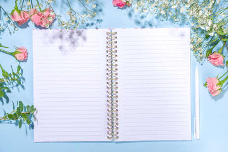 Cute spring flatlay with flowers and green spring leaves, high-colored bright sunny blue background with clean notepad pages for your text, top view frameの写真素材