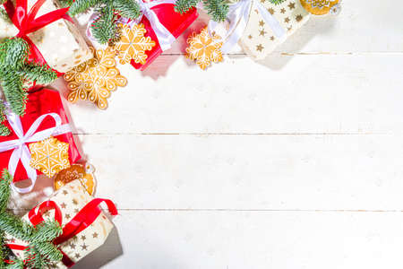 Traditional Christmas greeting card background. White and red gift boxes with festive ribbons, homemade gingerbread cookies and Christmas tree branches, on white wooden background copy spaceの写真素材