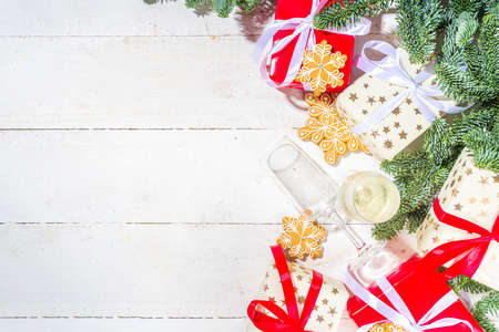 Traditional Christmas greeting card background. White and red gift boxes with festive ribbons, homemade gingerbread cookies and Christmas tree branches, on white wooden background copy spaceの写真素材