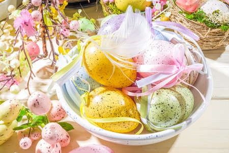 Easter painted colorful pastel eggs in a basket, with feathers on a light wood background. Easter...