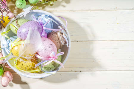 Easter painted colorful pastel eggs in a basket, with feathers on a light wood background. Easter...