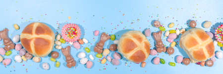 Bright high-colored Easter festive background. Blue background with traditional Easter sweets - hot cross buns, chocolate eggs sweets, colorful sugar sprinkles flatlay copy spaceの写真素材