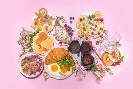 Valentine day brunch menu background with various breakfast and lunch dishes, waffle, growing, muffins, donuts, berries, fries scrambled eggs, pancakes, pink background copy spaceの写真素材