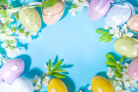 Happy Easter Spring Holiday Greeting Card Background with Easter colorful eggs, decorative bird nests and blossom spring garden flowers, flatlay copy space on high-colored blue backgroundの写真素材