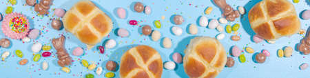 Bright high-colored Easter festive background. Blue background with traditional Easter sweets - hot cross buns, chocolate eggs sweets, colorful sugar sprinkles flatlay copy spaceの写真素材
