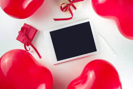Valentine day sweet holiday background with red heart shaped balloons on red background, with notepad, tablet, flatlay top view frame copy space, mockup for Valentine's greeting cardの写真素材