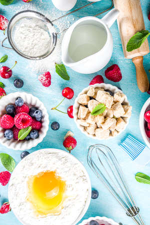 Berry cake baking recipe. Summer cooking baking background with assorted berries, baking ingredients, tools and utensils, light blue sun lighted wooden background flat lay top view copy spaceの写真素材