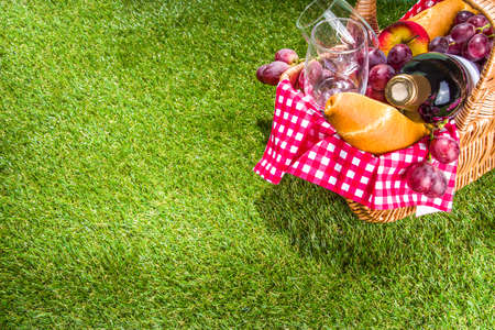 Picnic basket with food, wine bottle, glasses and fruits on green sunny lawn grassの写真素材