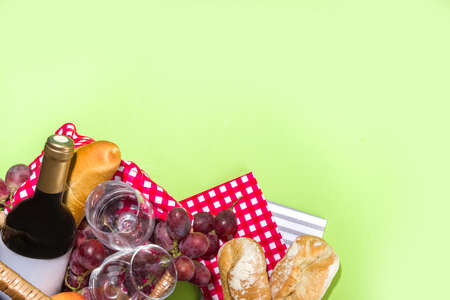 Picnic basket with food, wine bottle, glasses and fruits on green sunny lawn grassの写真素材