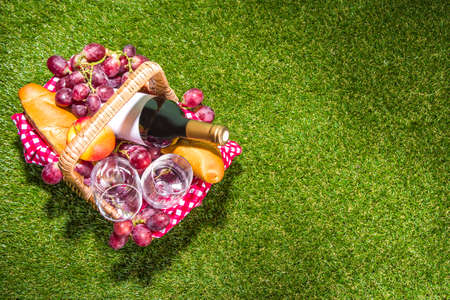 Picnic basket with food, wine bottle, glasses and fruits on green sunny lawn grassの写真素材