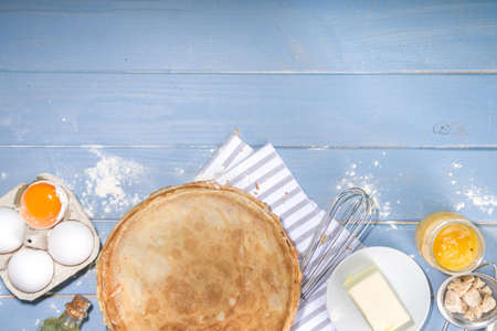 Russian Ukrainian European holiday Maslenitsa. Traditional thin crepes pancakes, on wooden blue table with ingredients for cooking - flour, eggs, butter, top view copy spaceの写真素材