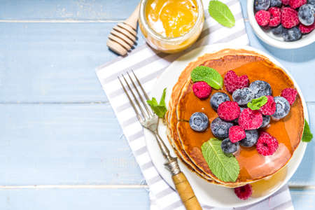 Plate of delicious traditional american pancakes with fresh berries and syrup on kitchen table on...