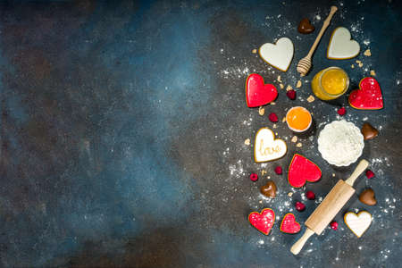 Valentine day sweet cooking background. Baking ingredients and utensils - flour, rolling pin, heart shaped biscuits, eggs. Making cute Valentine`s sweet gift. Top view copy space on dark blue backgroundの写真素材