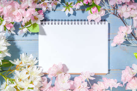 hello spring concept. Spring holidays greeting card simple flatlay background with artificial blossom spring flowers on light blue wooden garden table background frame copy space top viewの写真素材