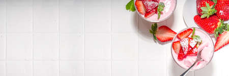 Homemade sweet strawberry panna cotta dessert, pink Italian panna cotta in three glasses, with fresh sliced strawberry and mint on white tiled background copy spaceの写真素材