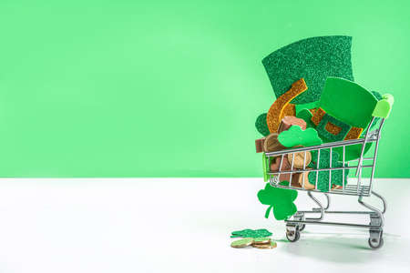 St Patrick sale background, supermarket shopping trolley with shamrock clover leaves, leprechaun hat decor, golden coins and chocolates in form of symbol of st. patrician dayの写真素材