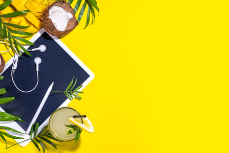Simple high-colored summer holiday background. Tablet with empty screen with tropical cocktail, summer fruits, palm leaves, on bright yellow background. Travel, vacation flat lay top view copy spaceの写真素材