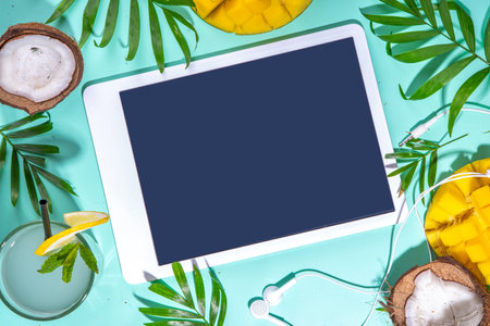 Simple high-colored summer holiday background. Tablet with empty screen with tropical cocktail, summer fruits, palm leaves on water colored blue background. Travel vacation flat lay top view copy spaceの写真素材
