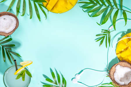 Tropical summer background with hat, mango, coconut tropical fruits, palm leaves, headphones. Summer...