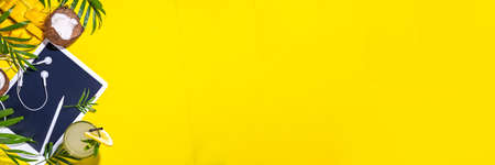Simple high-colored summer holiday background. Tablet with empty screen with tropical cocktail, summer fruits, palm leaves, on bright yellow background. Travel, vacation flat lay top view copy spaceの写真素材