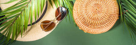 Summer simple modern minimal background. Palm tree tropical leaves, with a woman's hat, wicker straw bag, sunglasses. On a dark green background, flat lei with a bright sun, top view copy spaceの写真素材