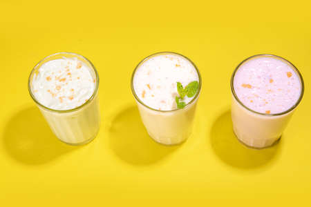 Refreshing yogurt, milkshakes or smoothies. Three glasses with fruit milkshakes. White banana, green apple avocado, yellow mango tropical fruits smoothie. On bright yellow table, copy spaceの写真素材