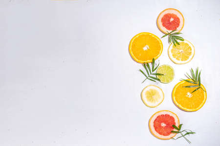 Colorful flatlay of citrus fruit slices and tropical palm leaves. Orange, grapefruit, lemon, lime bright high-colored slices on white background. summer holiday background top viewの写真素材
