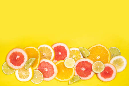 Colorful flatlay of citrus fruit slices and tropical palm leaves. Orange, grapefruit, lemon, lime bright high-colored slices on yellow background. summer holiday background top viewの写真素材