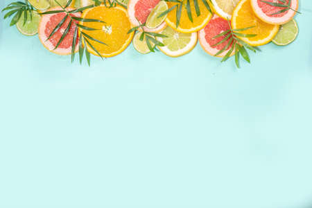 Colorful flatlay of citrus fruit slices and tropical palm leaves. Orange, grapefruit, lemon, lime bright high-colored slices on turquoise blue background. summer holiday background top viewの写真素材