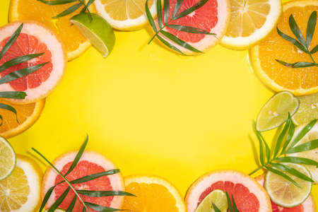 Colorful flatlay of citrus fruit slices and tropical palm leaves. Orange, grapefruit, lemon, lime bright high-colored slices on yellow background. summer holiday background top viewの写真素材