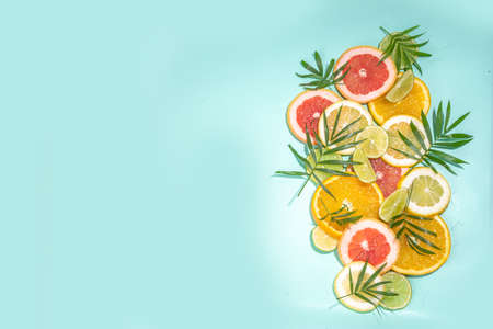 Colorful flatlay of citrus fruit slices and tropical palm leaves. Orange, grapefruit, lemon, lime bright high-colored slices on turquoise blue background. summer holiday background top viewの写真素材