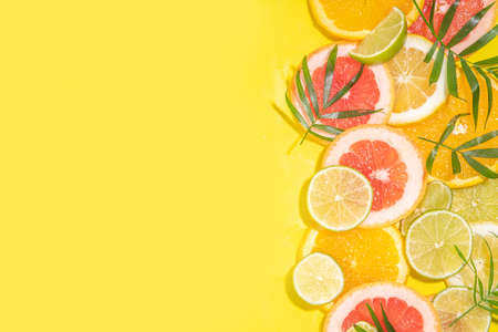 Colorful flatlay of citrus fruit slices and tropical palm leaves. Orange, grapefruit, lemon, lime bright high-colored slices on yellow background. summer holiday background top viewの写真素材