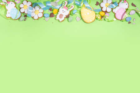 Happy Easter colorful flatlay. Colorful sugared and chocolate Easter eggs, sugar glazed cookies with festive holiday ribbon on light green background top view copy spaceの写真素材