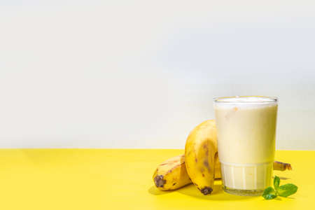 Banana smoothie, yogurt or milkshake cocktail, organic healthy drink with fresh bananas on yellow bright background copy spaceの写真素材