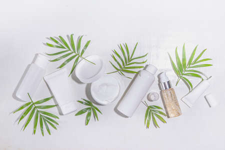 Beauty cosmetic skincare products on white background with tropical palm leaves flatlay copy space. Set of white jars, tubes, droppers and bottles. Summer spa, daily natural skin care routine conceptの写真素材