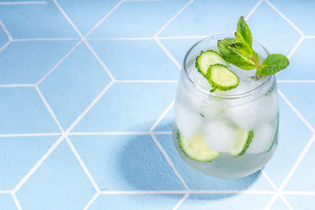 Refreshing summer drink - detox mint, cucumber, lemon cocktail. On light blue tiled table, bright sunlight, copy space. Two glass with cucumber infused water or lemonade, healthy diet drinkの写真素材